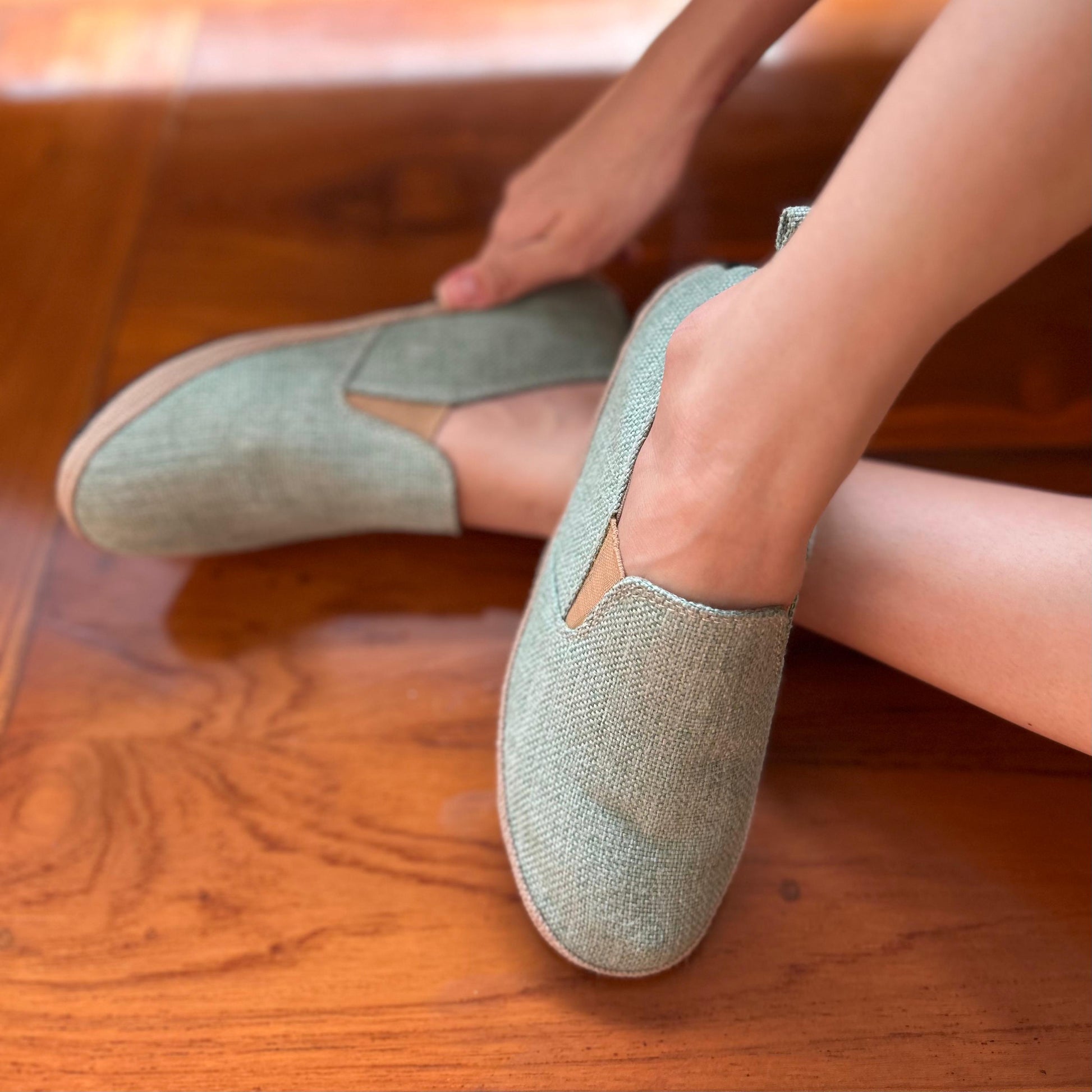 A person's feet wearing white hemp slip-on shoes with a white in the background.